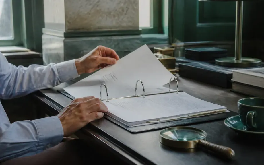 An open ring binder with tabbed dividers beside a magnifying glass