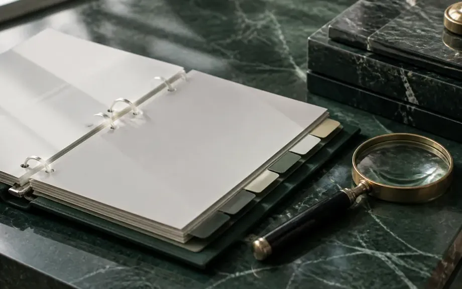 An open ring binder with tabbed dividers beside a magnifying glass
