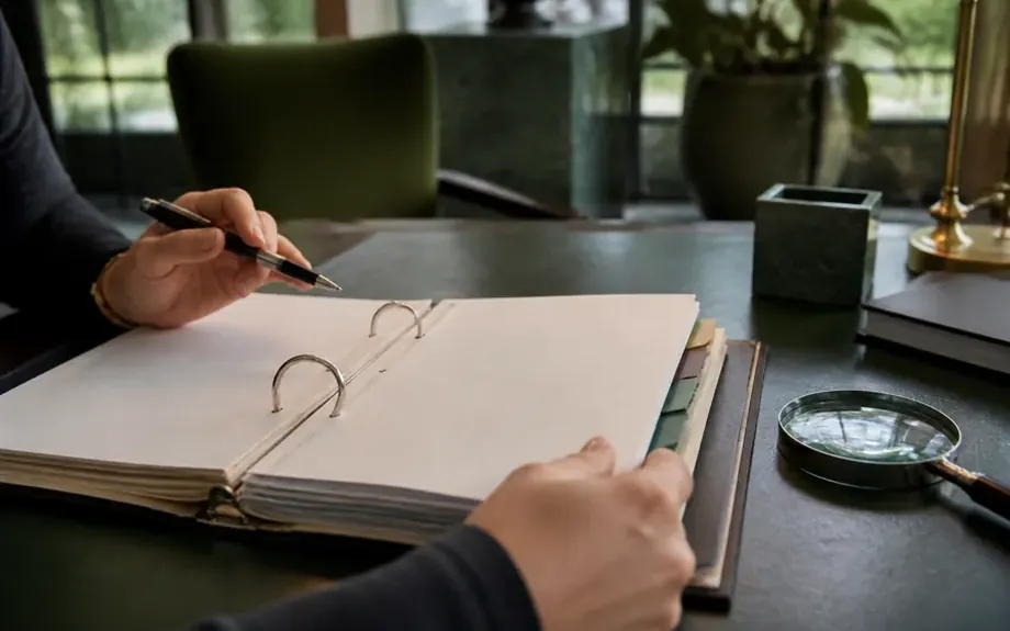An open ring binder with tabbed dividers beside a magnifying glass